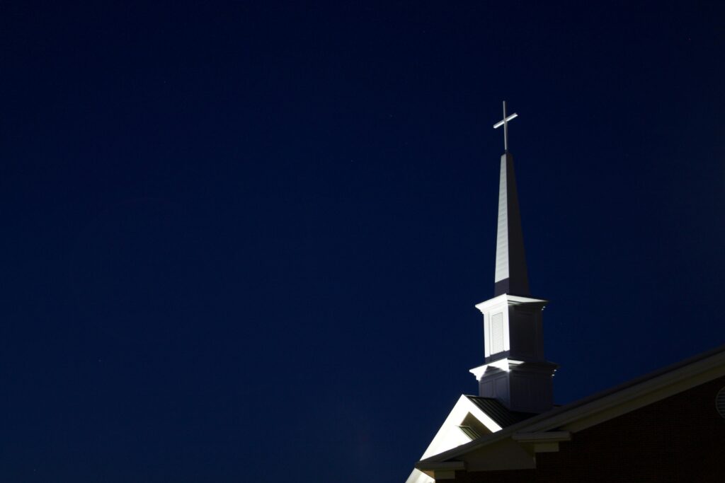 Illuminated church steeple with cross at night. Perfect for religious and architectural themes.